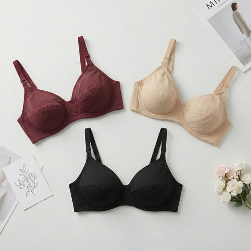Three bras in maroon, beige, and black on a light surface with flowers and a magazine.