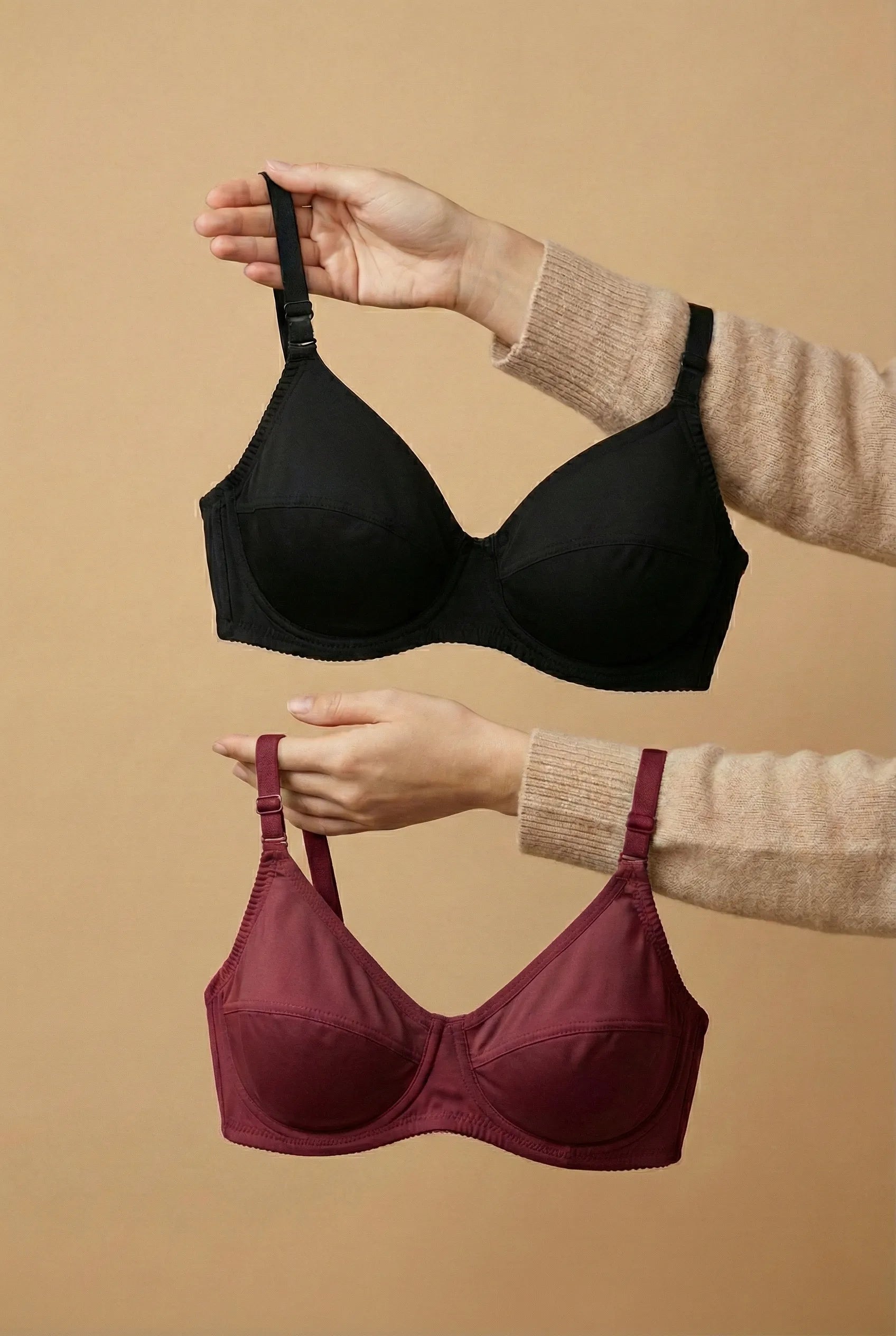 Black and Maroon bras held by a person against a beige background