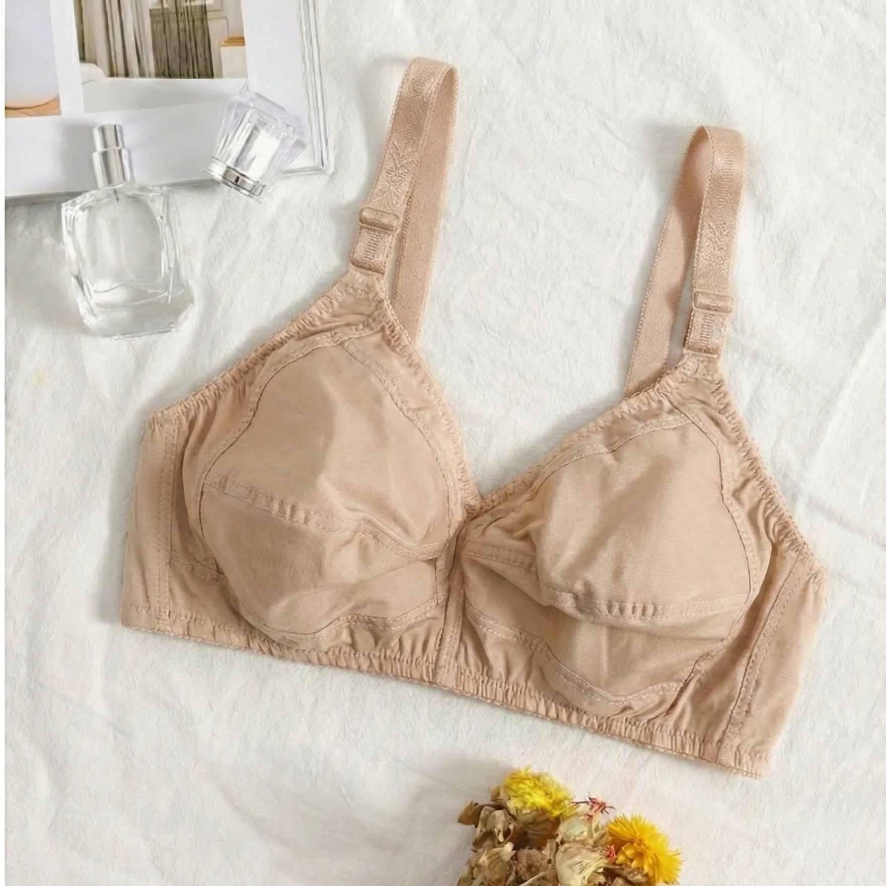 Beige bra on a textured white surface with flowers and a bottle in the background