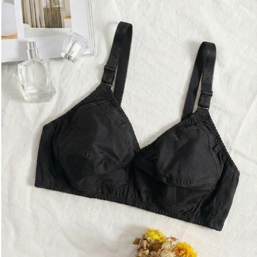 Black bra on a white surface with flowers and a bottle in the background