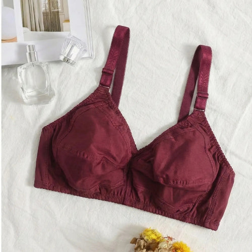 Maroon bra on a white surface with flowers and a bottle in the background